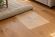 Tappeto beige parzialmente arrotolato su parquet con una zona più chiara rispetto al legno circostante