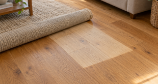 Tappeto beige parzialmente arrotolato su parquet con una zona più chiara rispetto al legno circostante